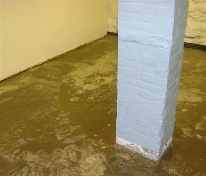muddy silt on the floor of a basement with a gray brick support column