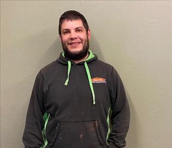 male employee in a black hoodie in front of a tan wall