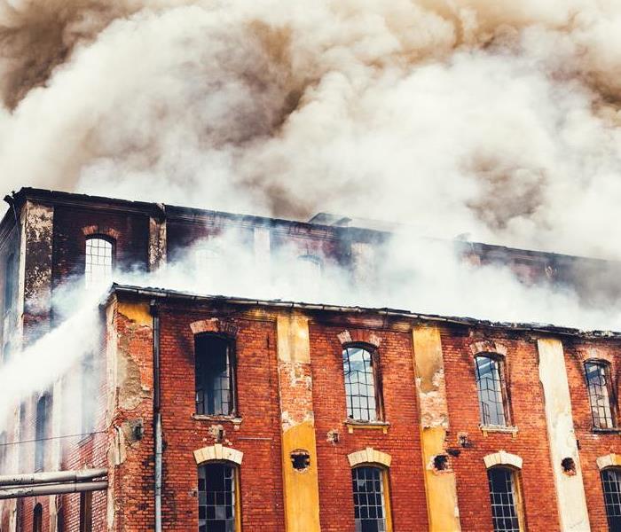 A building with fire and smoke blowing out of windows.